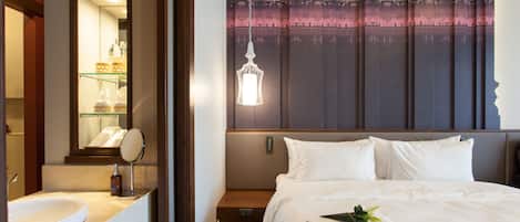 Habitación de hotel con una cama grande, una mesita de noche, un espejo y un baño con lavamanos y estantes.