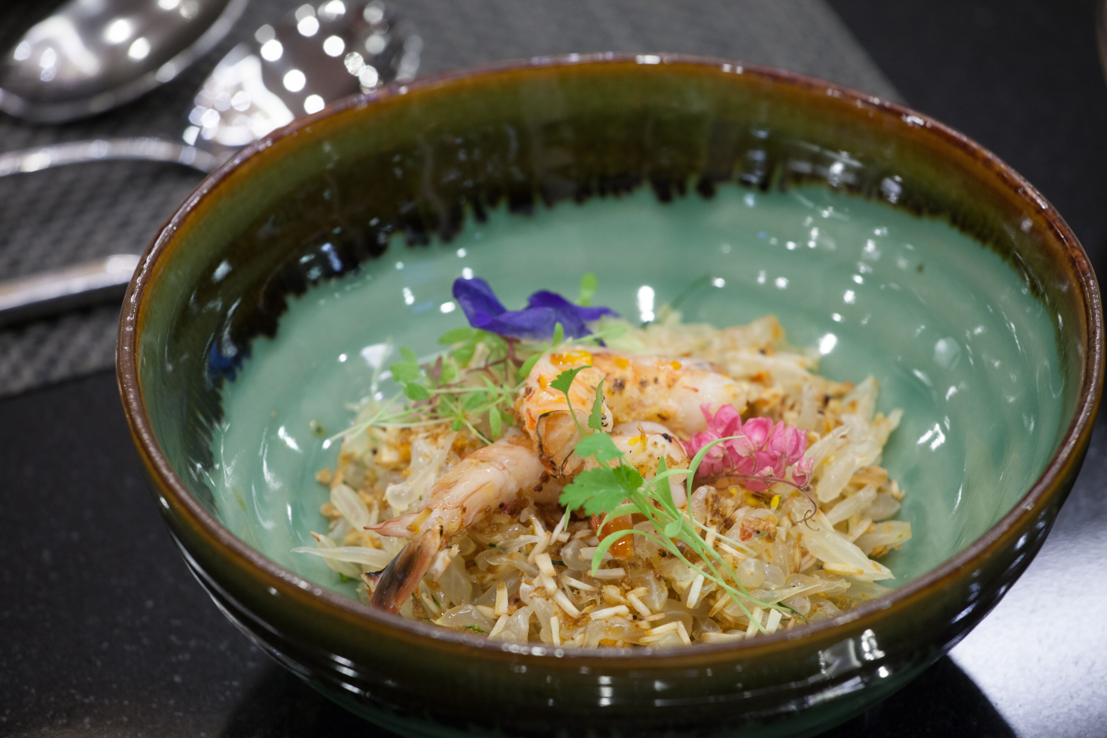 A bowl of food with rice, shrimp, and garnishes.