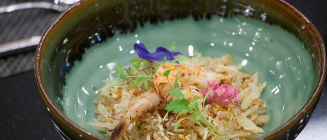A bowl of food with rice, shrimp, and garnishes.