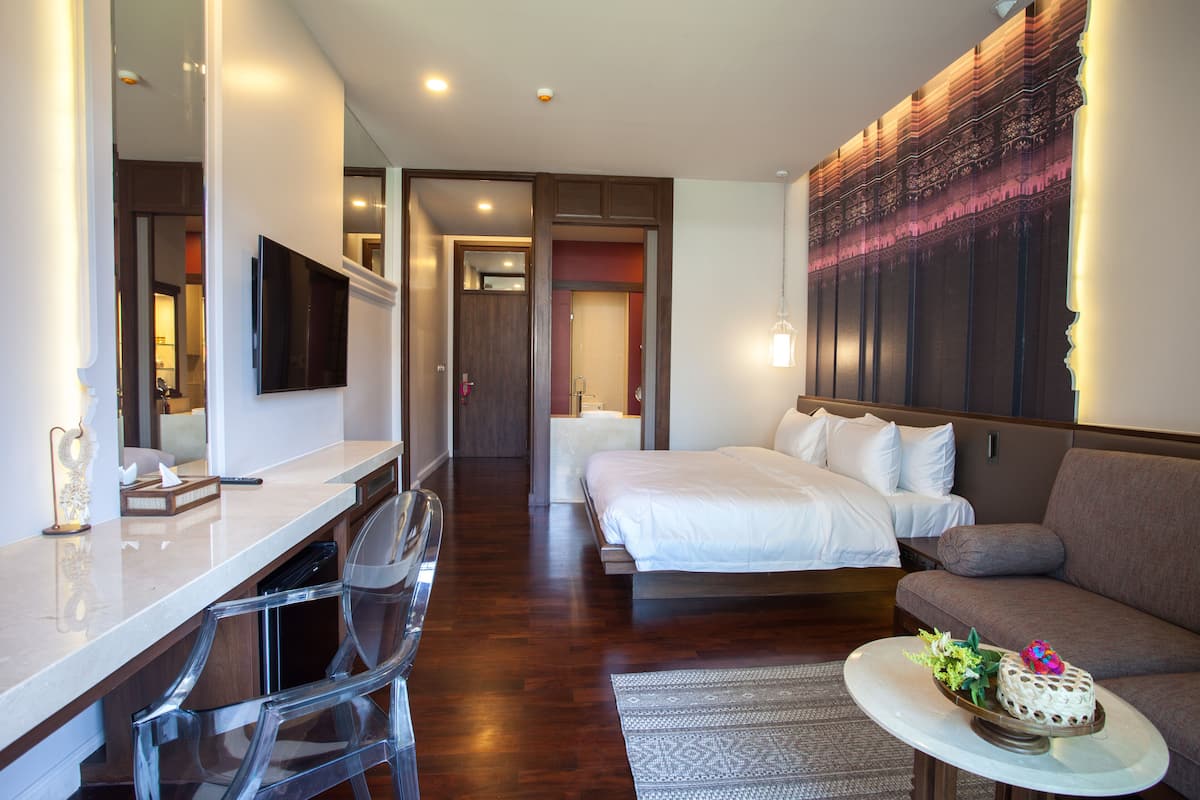 Une chambre d’hôtel avec un lit, un canapé, un bureau avec une chaise, une télévision et un gâteau décoratif posé sur une table.