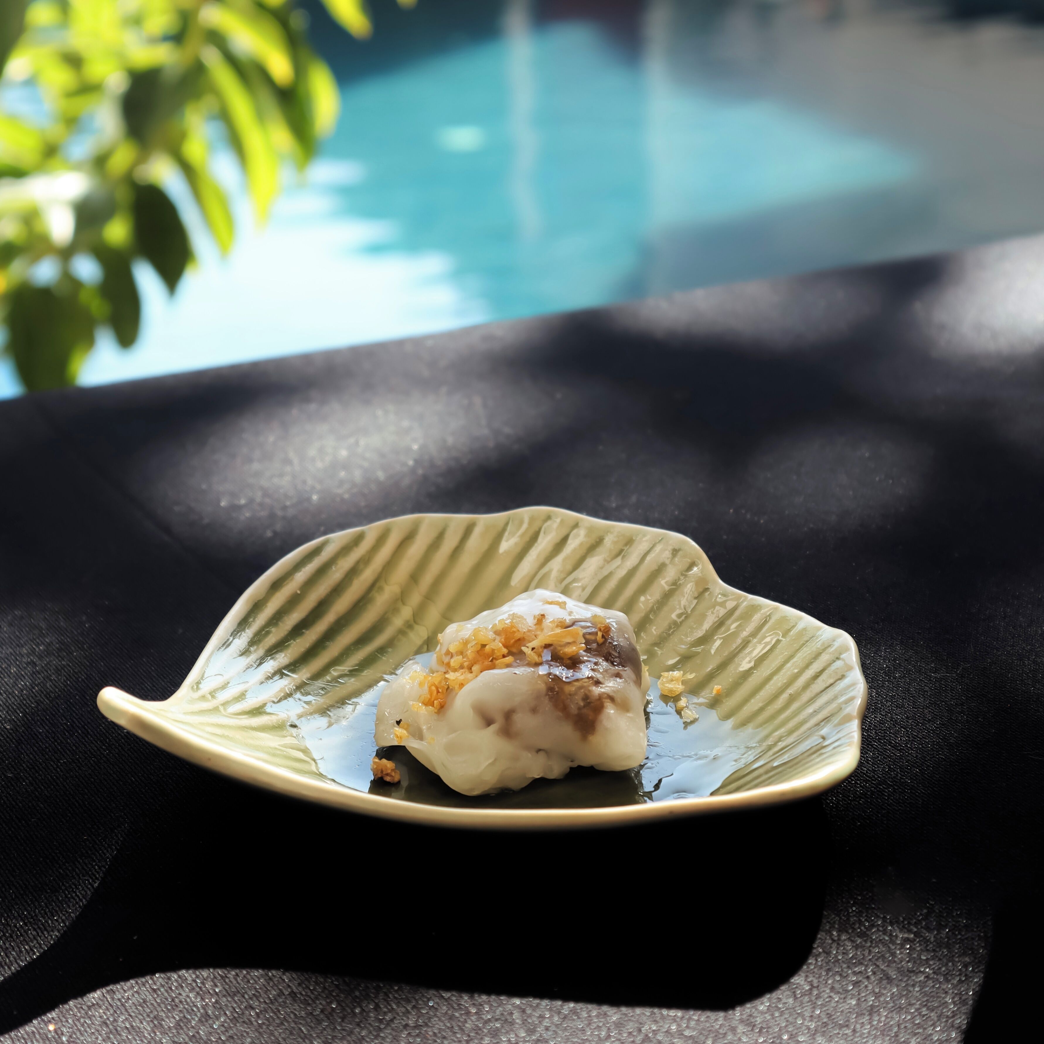A dish on a leaf-shaped plate with a pool in the background.