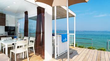 A modern outdoor dining area with a view of the sea, a covered seating area, and a kitchen with a TV.