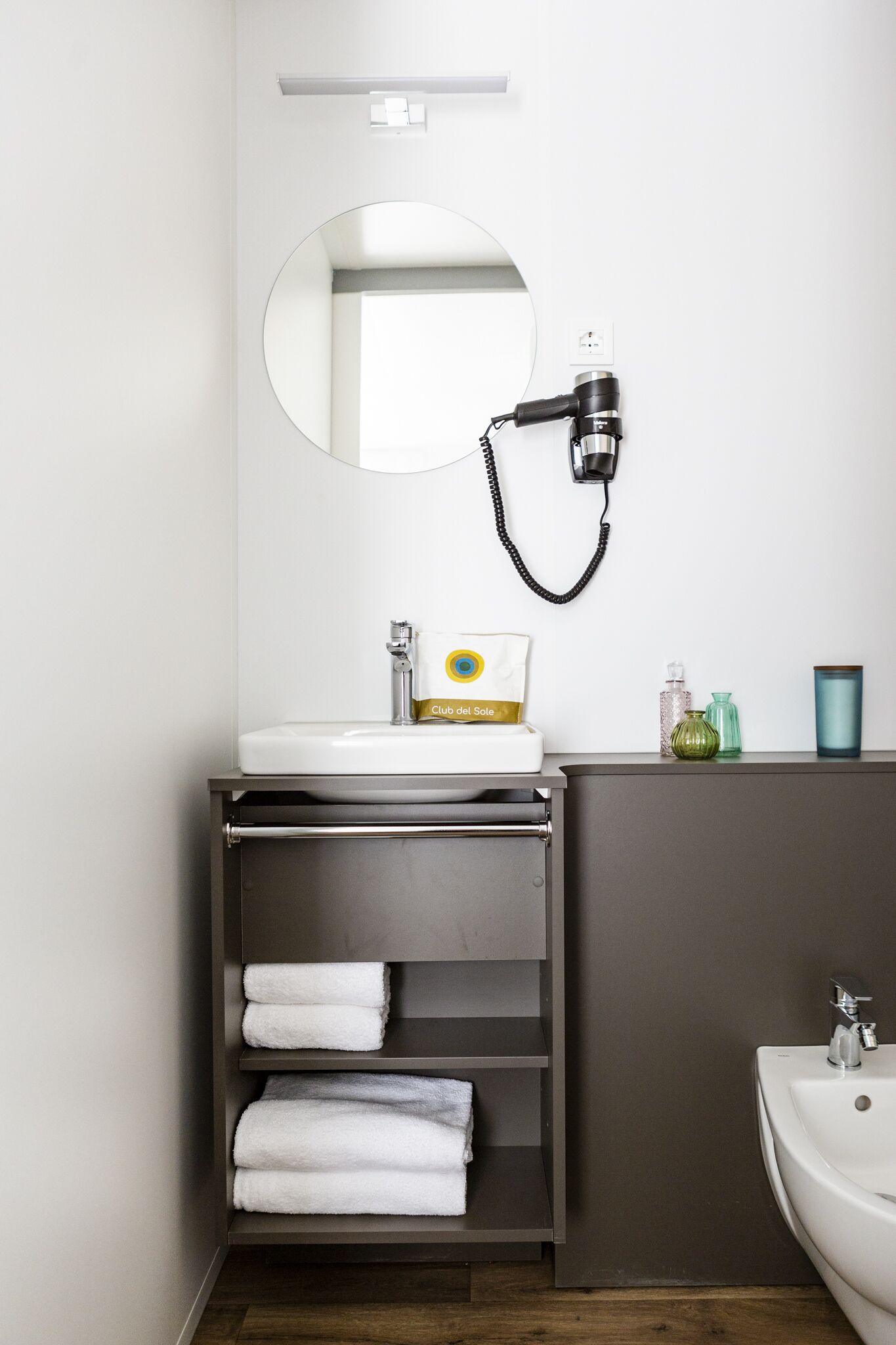 A bathroom with a white sink, a mirror, a hairdryer, a towel rack, and a bottle of shampoo.