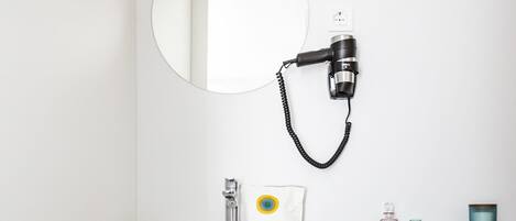 A bathroom with a white sink, a mirror, a hairdryer, a towel rack, and a bottle of shampoo.