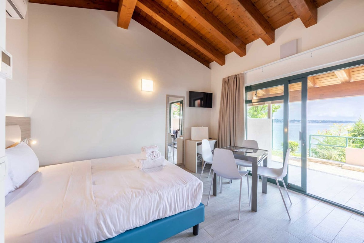 Un dormitorio con cama, escritorio y silla, televisor montado en la pared y un ventanal con vistas.