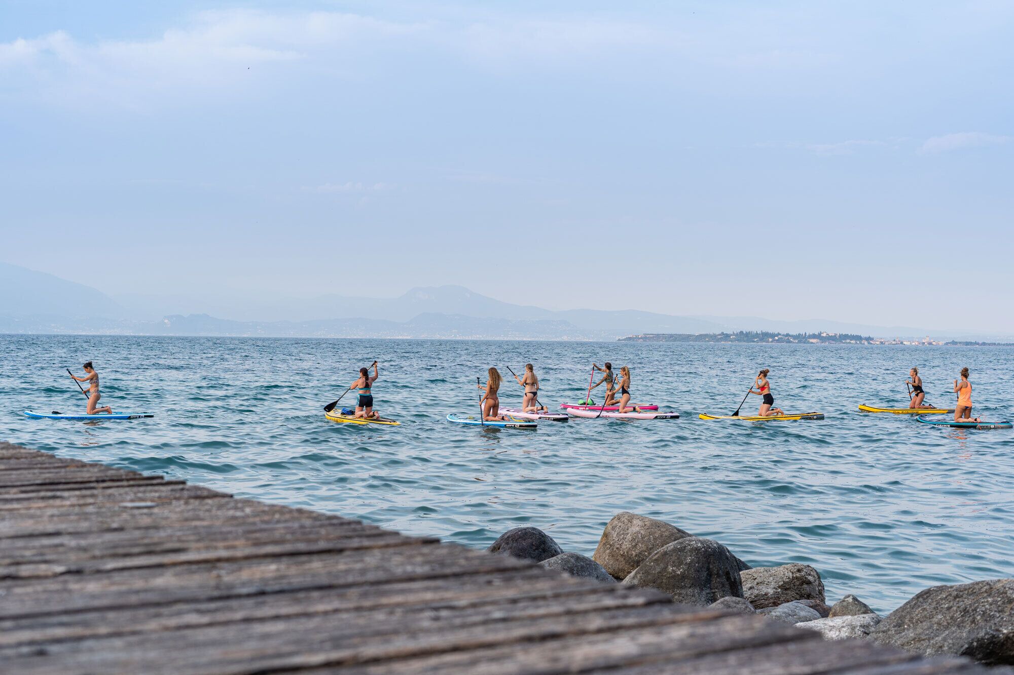 Un grupo de personas haciendo paddleboard en un mar tranquilo, con cielo despejado y montañas a lo lejos.