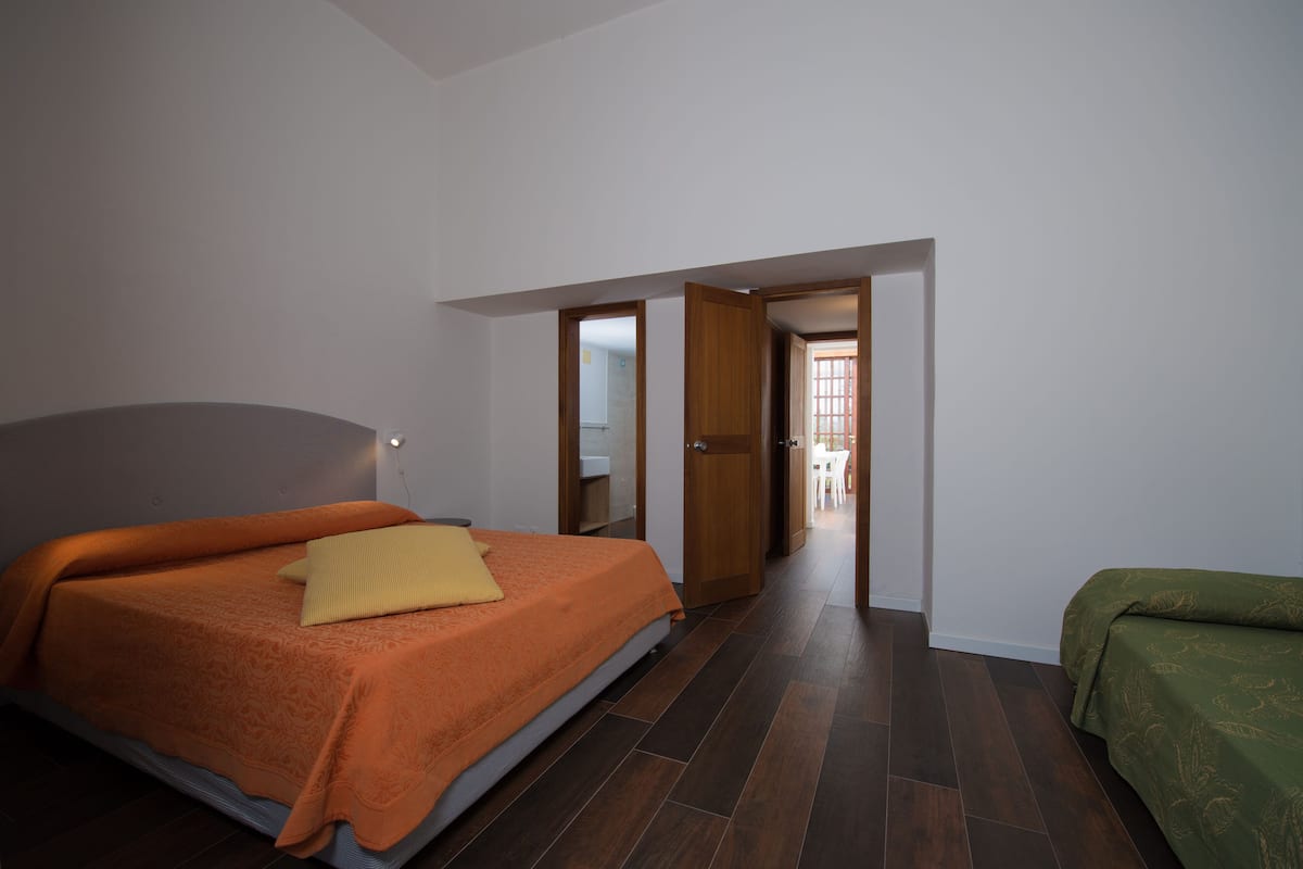 Un dormitorio con una cama, un sofá verde y una puerta de madera que da a otra habitación.