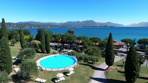 Ein runder Swimmingpool, umgeben von Liegestühlen und Sonnenschirmen, mit Blick auf einen See und Berge im Hintergrund.