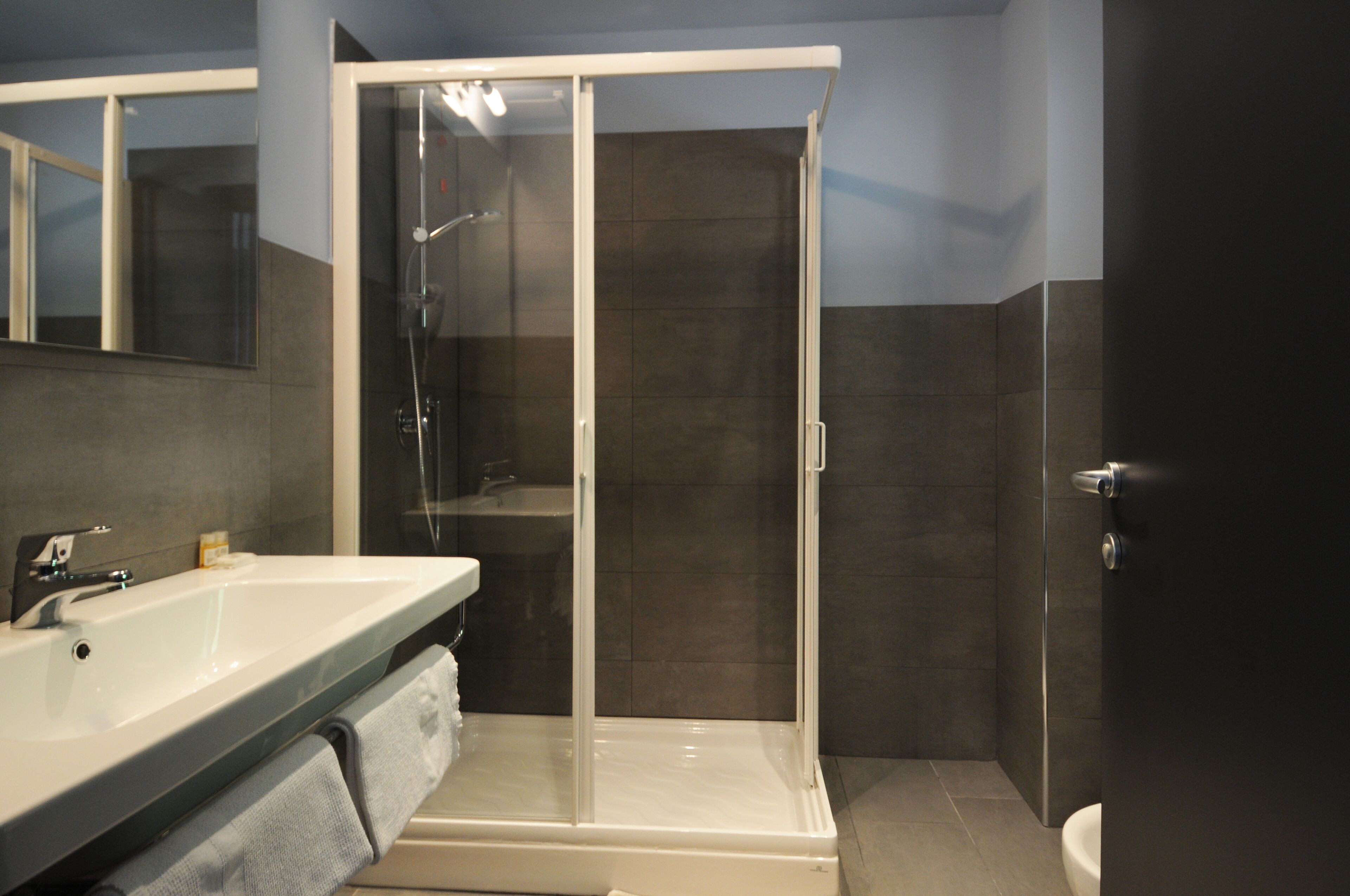 A modern bathroom with a glass-enclosed shower, a white sink, and a dark tiled wall.