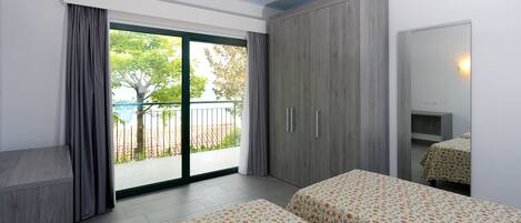 Un dormitorio con dos camas, un armario, un balcón con vistas y un ventanal grande.