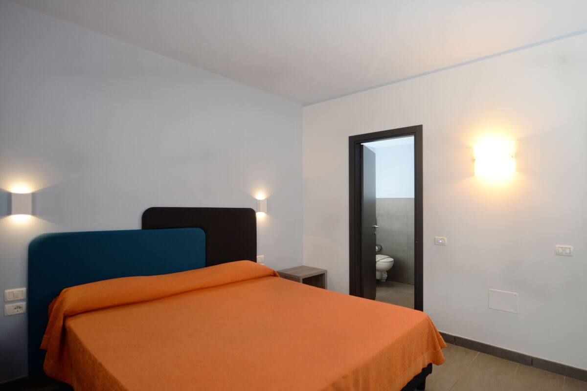 Una habitación de hotel con una cama, una mesita de noche, un espejo y una lámpara en la pared.