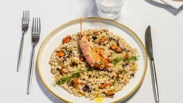A plate of seafood risotto with a shrimp centerpiece, accompanied by cutlery and a glass of water on a white tablecloth.