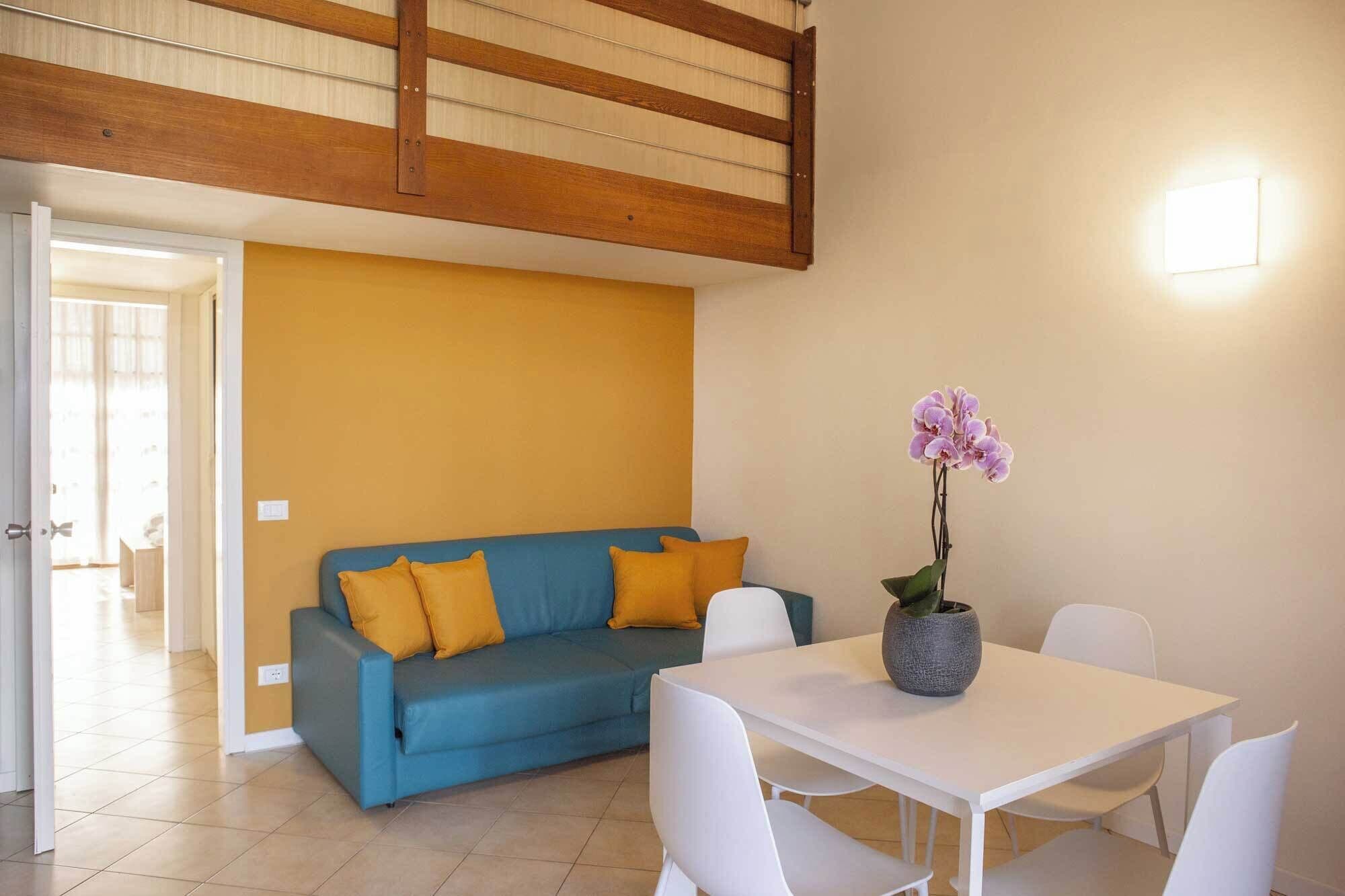 Una habitación con un sofá azul, sillas blancas, una mesa blanca y una orquídea en maceta.