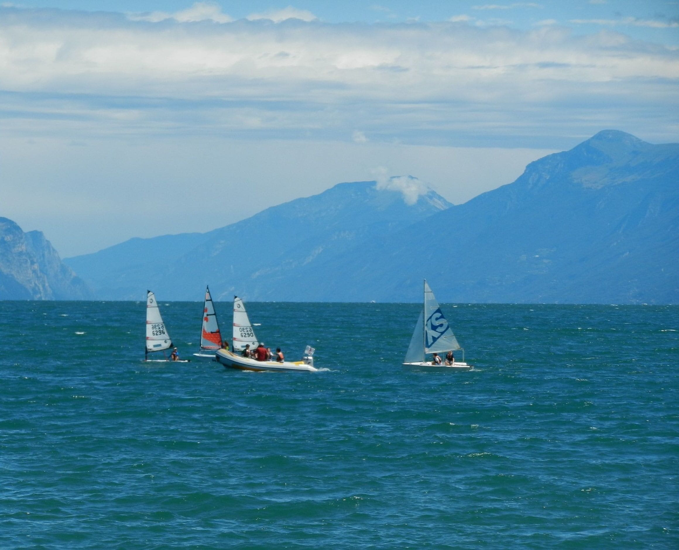 Una barca a vela con diverse vele su un corpo d'acqua, con montagne sullo sfondo.