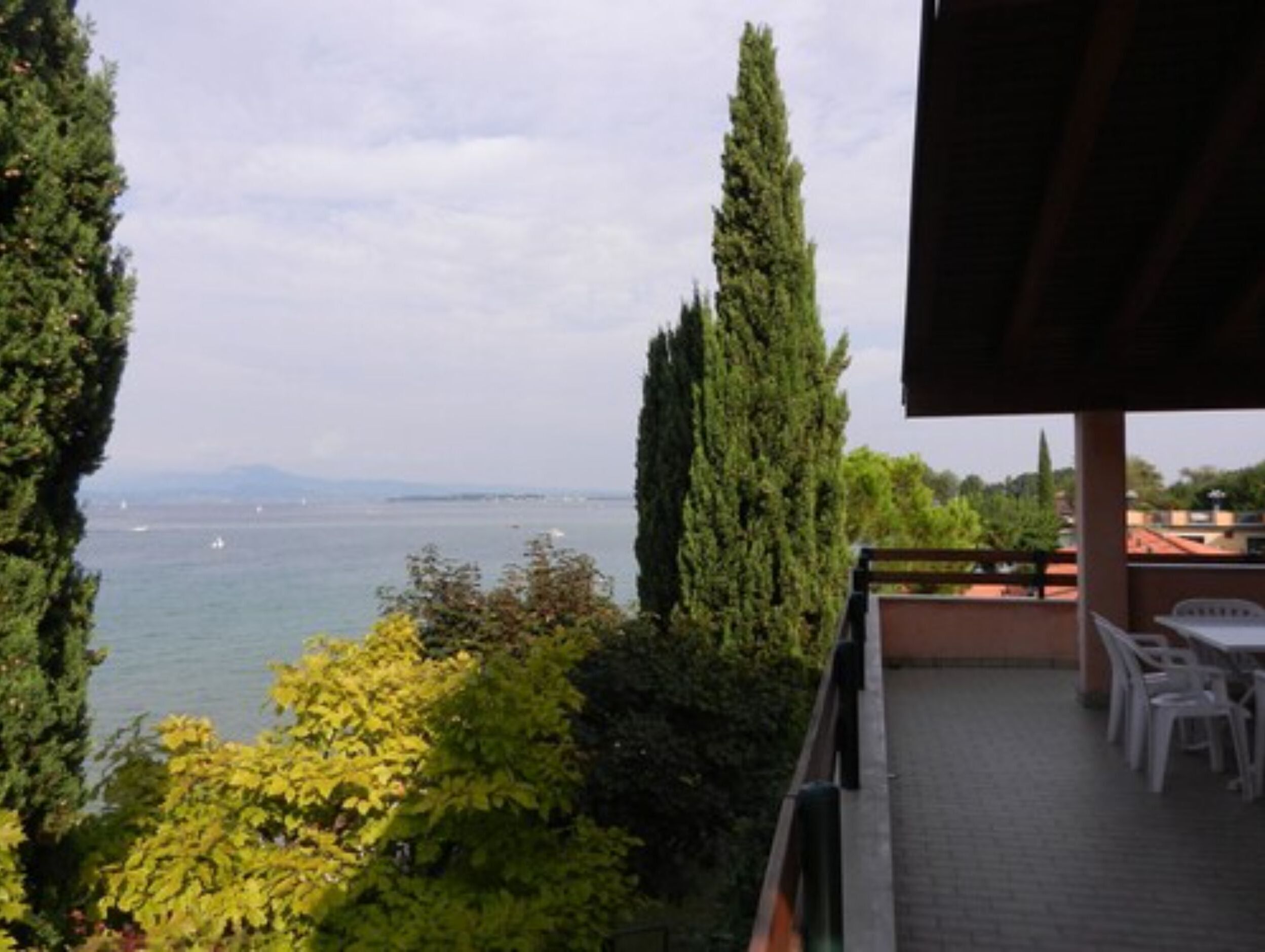 A terrace with a view of the sea, surrounded by greenery and a building structure.