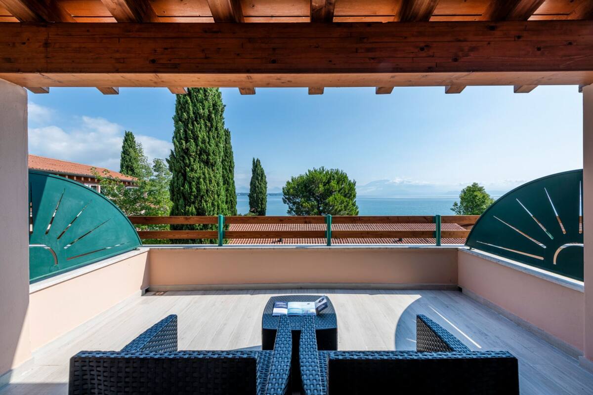 Un balcón con vista al mar, una pérgola de madera y una mesa con sillas.
