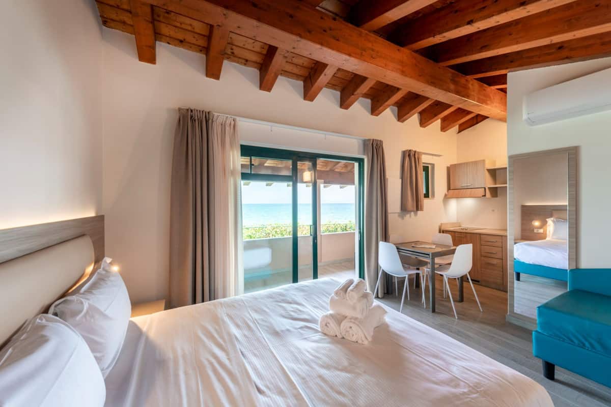 Habitación de hotel con una cama grande, un escritorio y vistas al mar a través de una puerta corrediza.