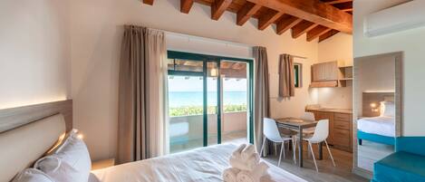 A hotel room with a large bed, a desk, and a view of the sea through a sliding door.