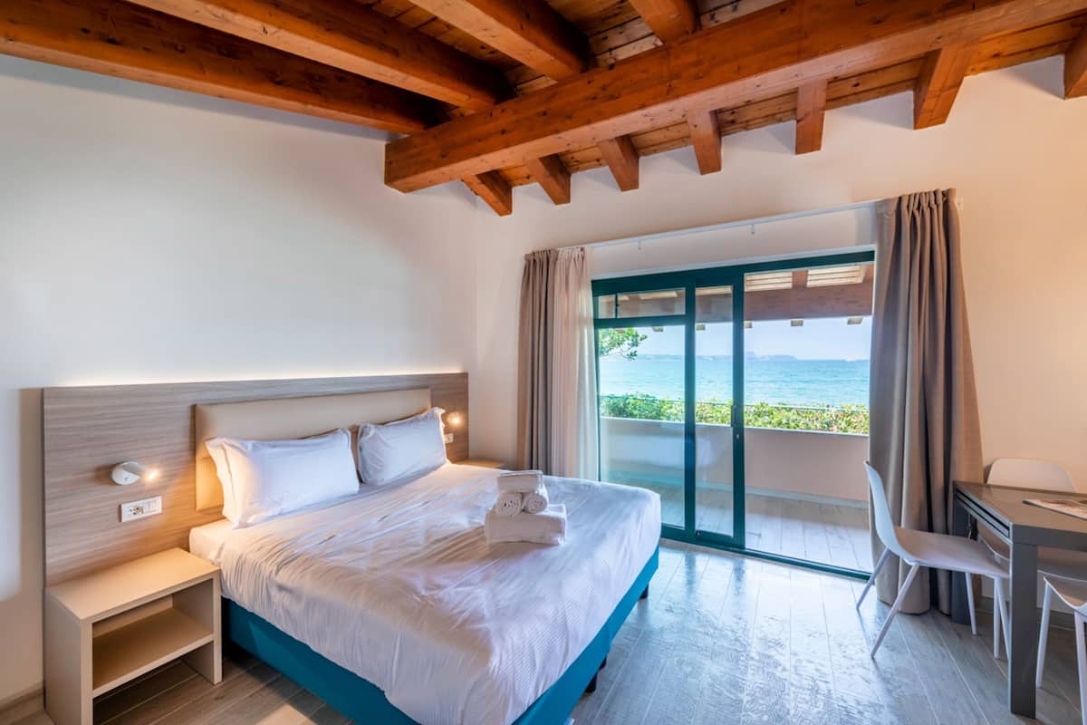 Un dormitorio moderno con una cama grande, una mesita de noche, un escritorio y vistas al mar a través de un ventanal corredero.