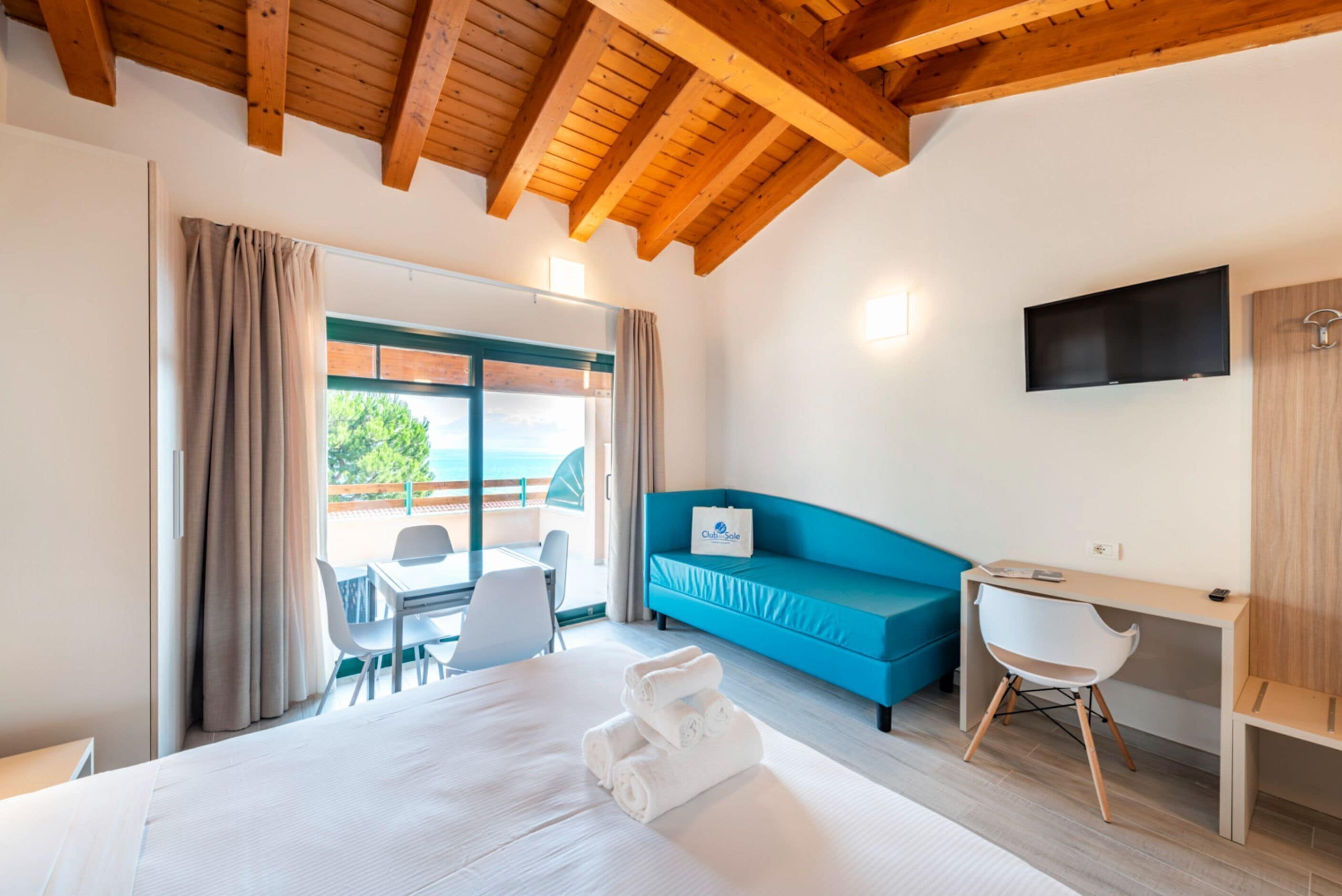 Una habitación de hotel con una cama, un sofá azul, un escritorio y un televisor.