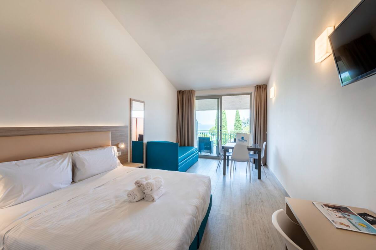 Habitación de hotel con una cama grande, un escritorio, una silla, un televisor y un balcón con vistas.