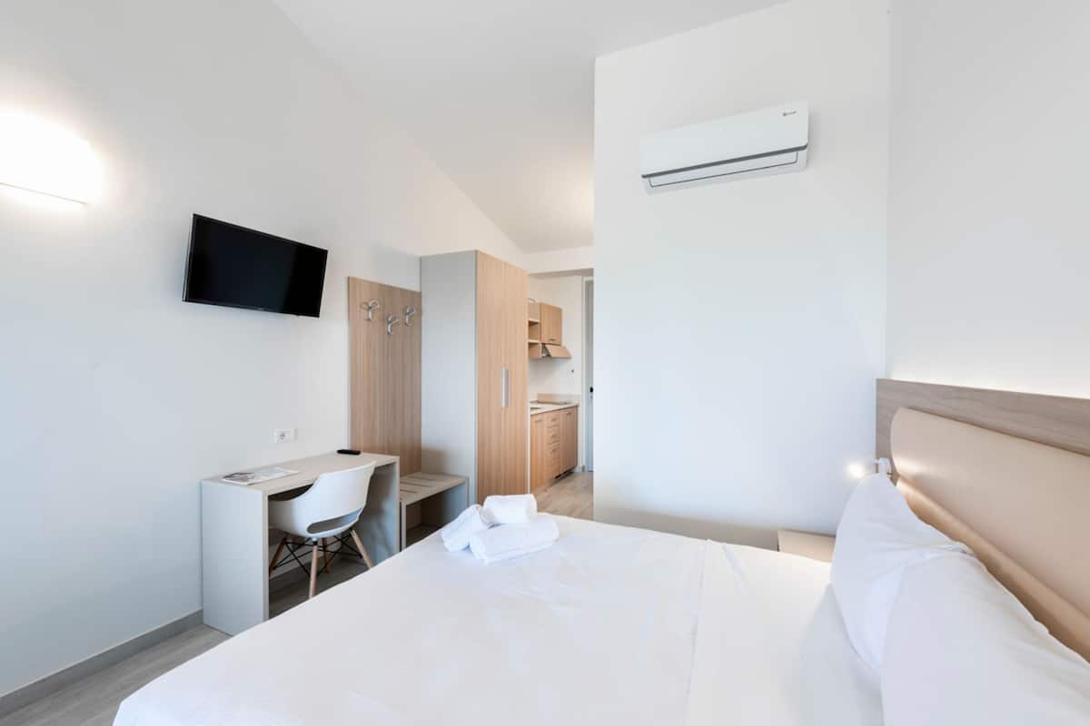 Una habitación de hotel moderna con cama, escritorio, silla, televisor y aire acondicionado.