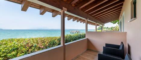 A covered balcony with wooden beams, a view of the sea, and wicker furniture.