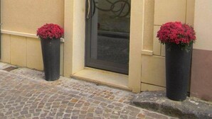 A building entrance with a glass door, two potted red flowers, and a sign on the wall. - Guesthouse San Domenico (Augusta)