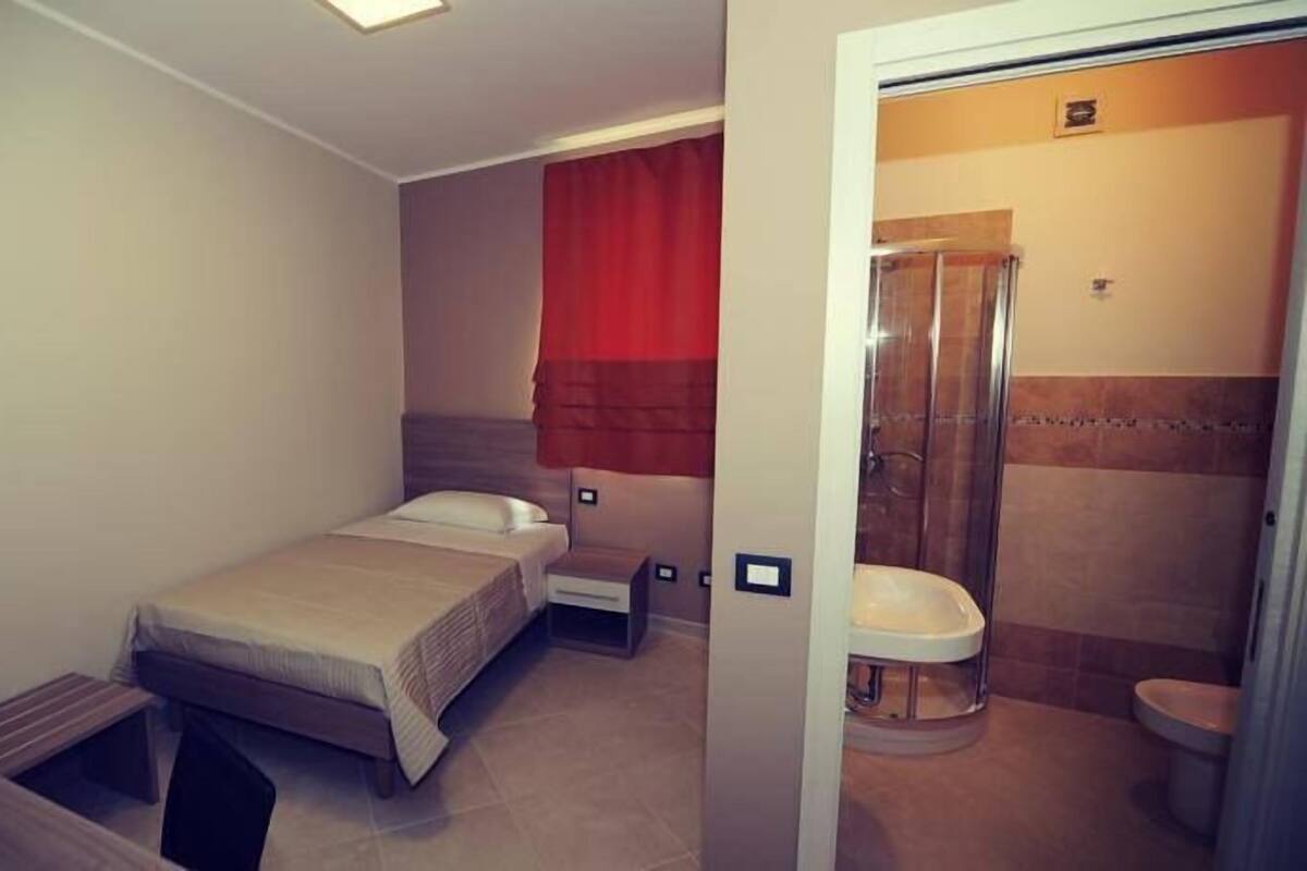 A hotel room with a bed, a desk, and a shower area.