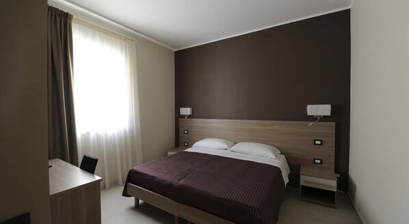 A hotel room with a large bed, two bedside tables, a desk, and a window with curtains. - Guesthouse San Domenico (Augusta)