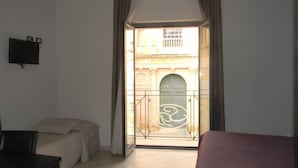 A hotel room with a bed, a desk, a TV, and a balcony with a view of a building. - Guesthouse San Domenico (Augusta)