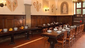 A dining hall with long wooden tables set for service, a stone column, and wall-mounted decorations including flags and a plaque. - Villa Palazzola (Albano Laziale)
