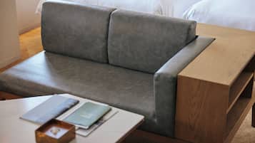 A modern room with a grey sofa, a wooden side table, and a bed with white linens.