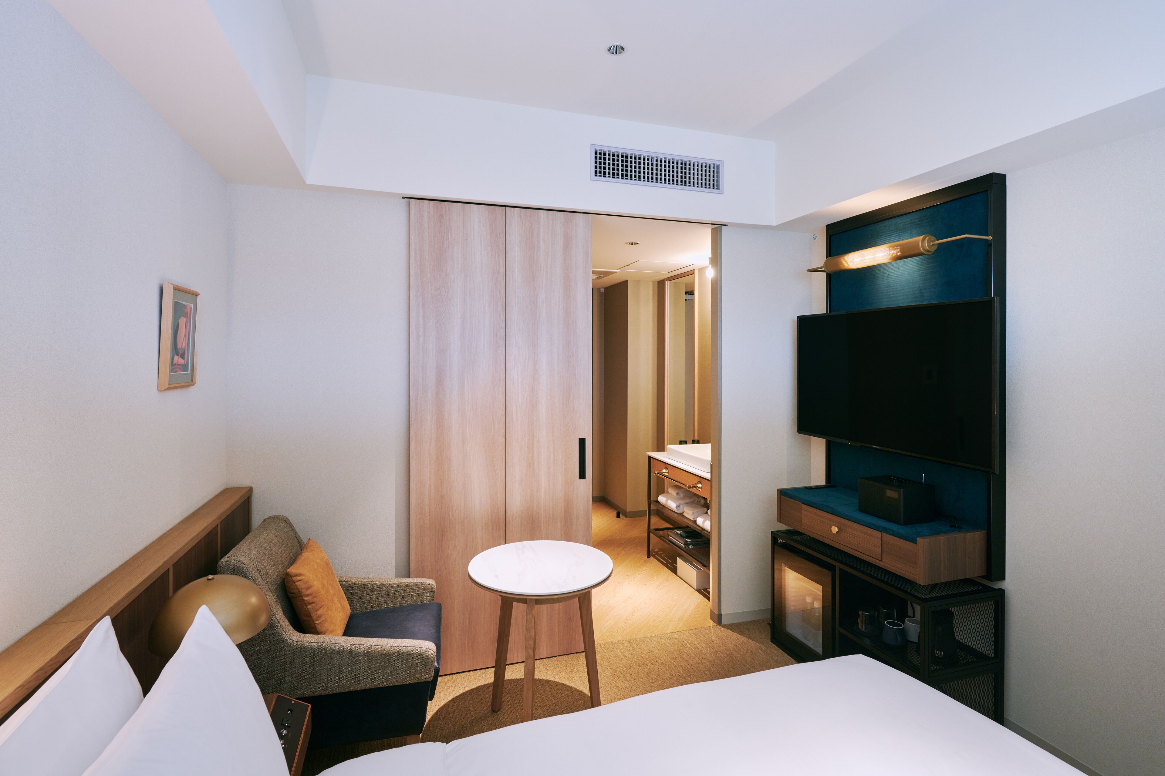 Une chambre d’hôtel comprenant un lit, une petite table ronde, un canapé, un téléviseur fixé au mur et un dressing.