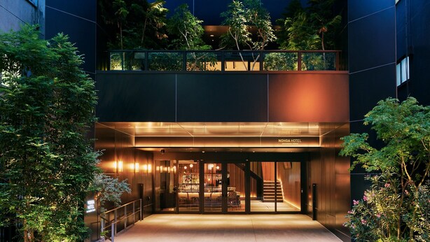 A modern hotel with a glass entrance, outdoor seating, and a rooftop garden.