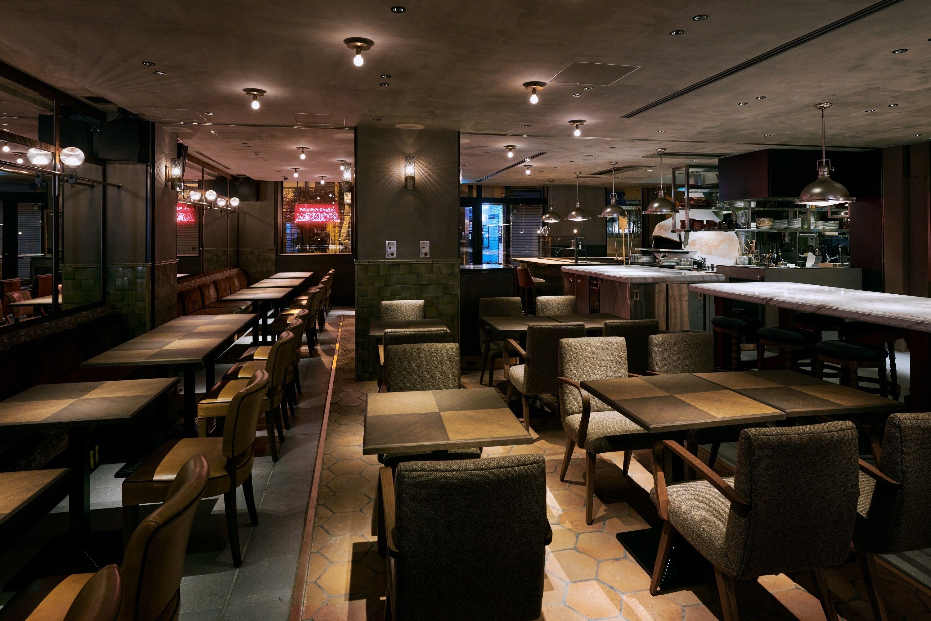 Un restaurant doté de nombreuses tables et chaises, d’un bar et d’une cuisine visible au fond de la salle.