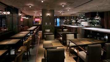 Un restaurant doté de nombreuses tables et chaises, d’un bar et d’une cuisine visible au fond de la salle.