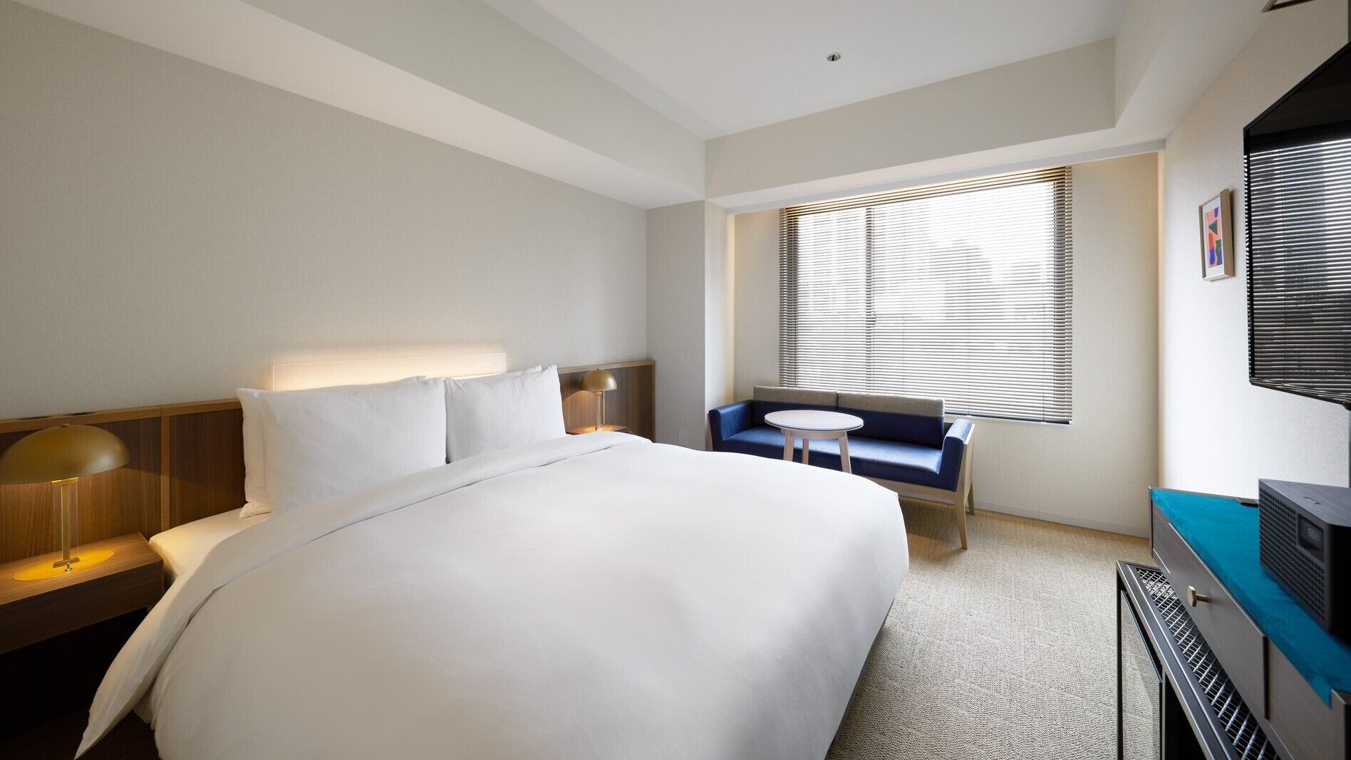 A hotel room with a large bed, a desk with a lamp, a small round table, a sofa, and a TV.