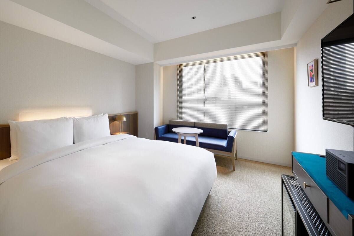 A hotel room with a large bed, a desk with a lamp, a small round table, a sofa, and a TV.