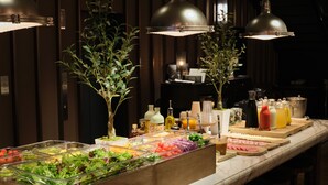 A buffet setup with various food items and condiments, including salads, fruits, and beverages, in a well-lit room with wooden paneling and pendant lights.