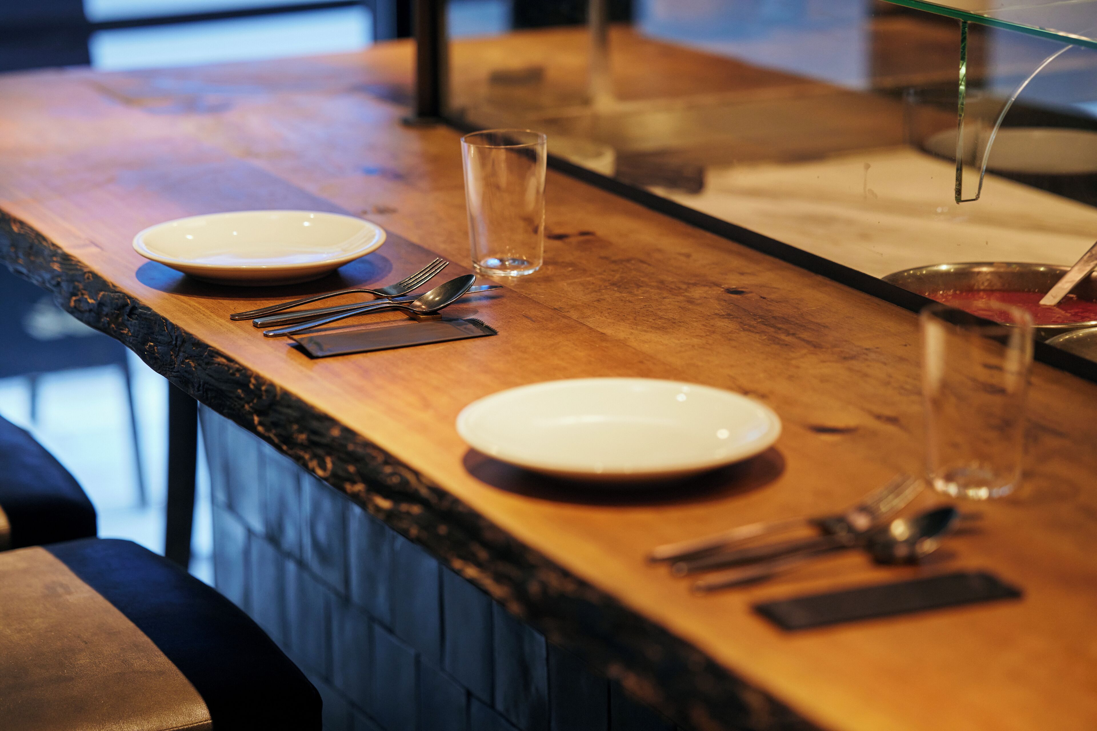 A restaurant counter with two plates, cutlery, and glasses.