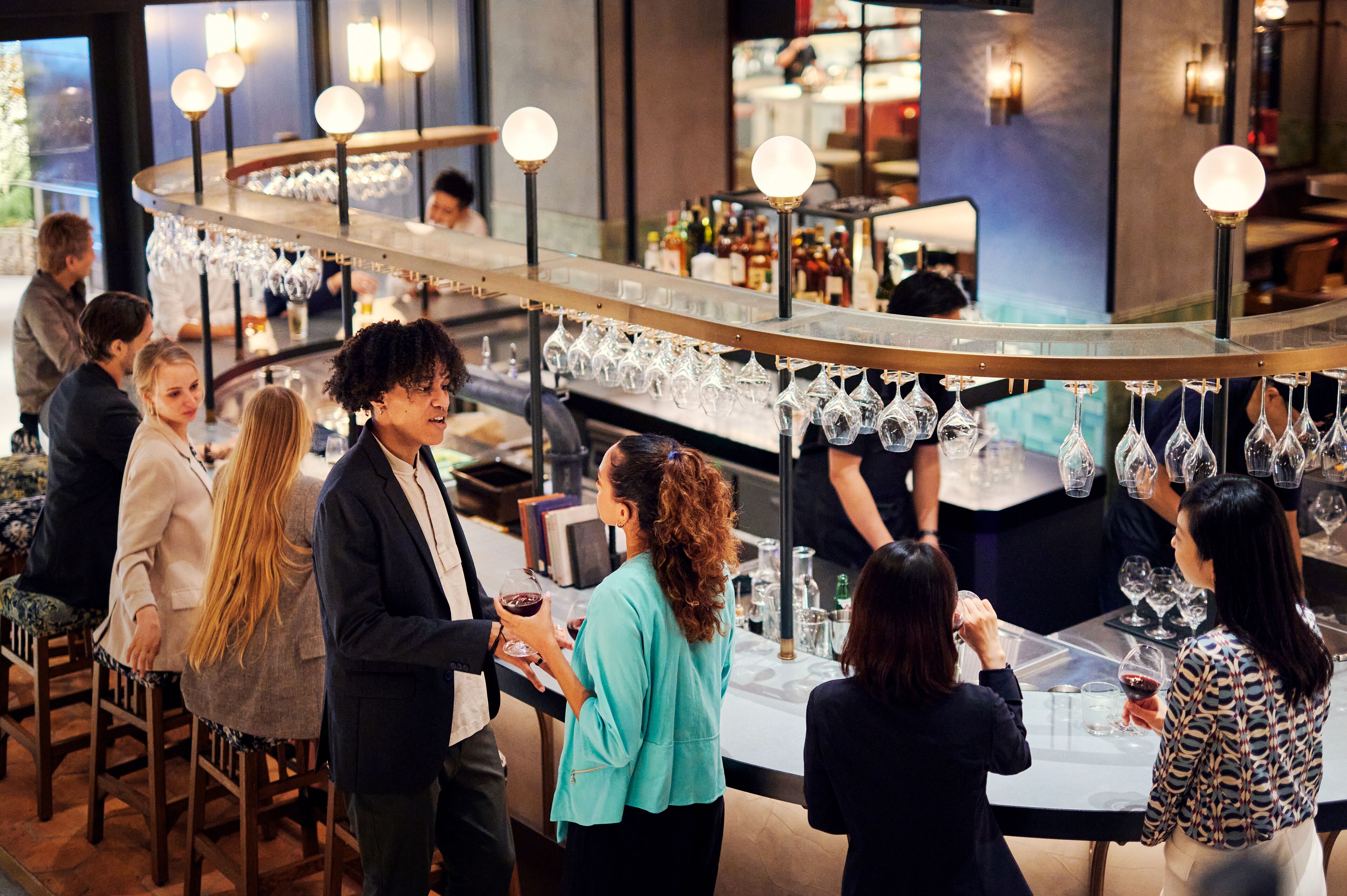 A bar area with a curved counter, hanging wine glasses, and a bartender.