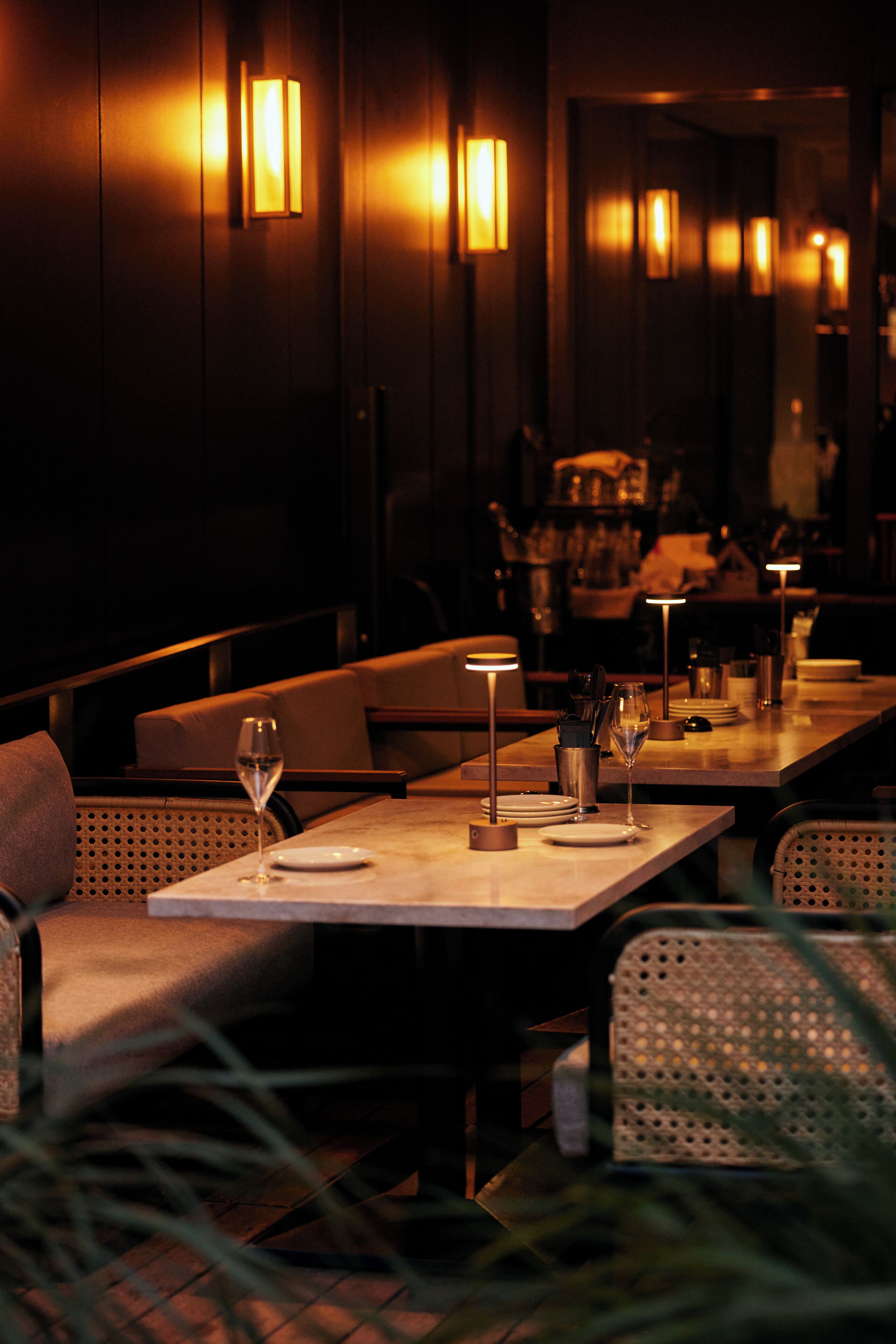 Un restaurant à la lumière tamisée, avec des tables dressées pour le dîner, doté d’un éclairage mural et d’une atmosphère chaleureuse.