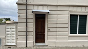 Fachada de edificio con puerta de madera, ventana con contraventanas y toldo blanco.