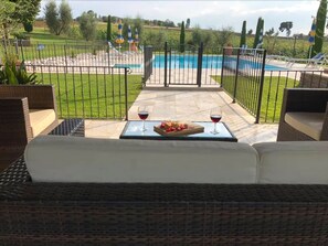 A patio with a view of a pool, outdoor furniture, and a table with wine glasses and fruit. - Rosa dei Venti (Cortona)