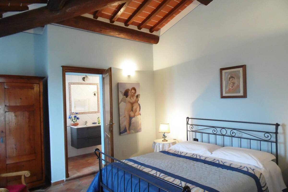 Un dormitorio con cama, mesita de noche, un cuadro y puerta de madera.