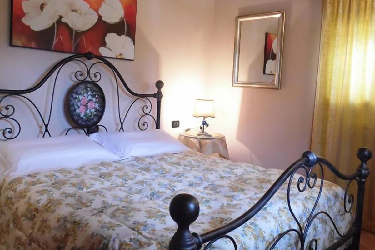 Un dormitorio con cama, ventilador de techo, un cuadro, lámpara y ventana con cortinas.