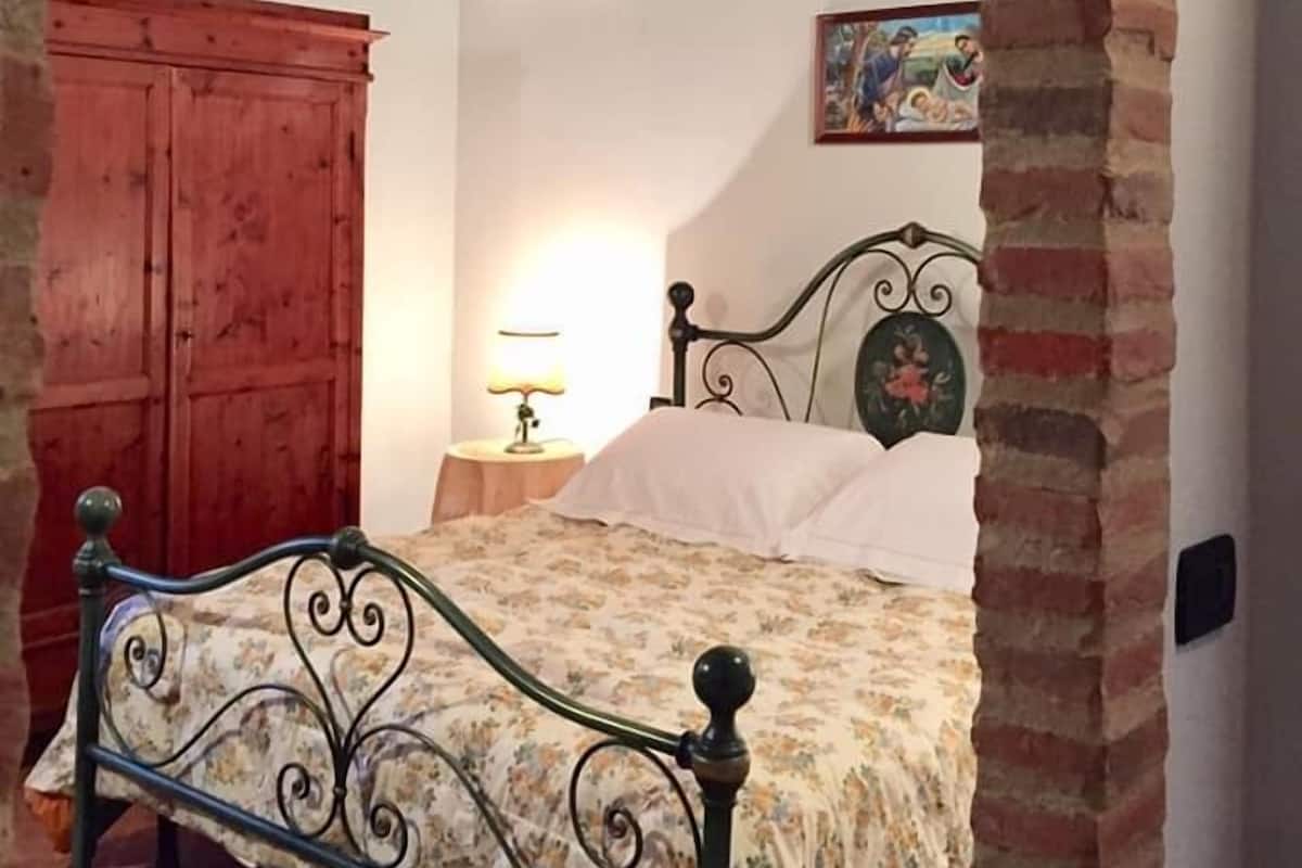 Un dormitorio con una cama, un armario de madera, un equipo de aire acondicionado, una lámpara y un cuadro en la pared.