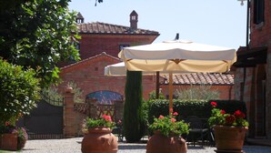 Un patio con un edificio de ladrillo, macetas de terracota con flores y un paraguas grande.