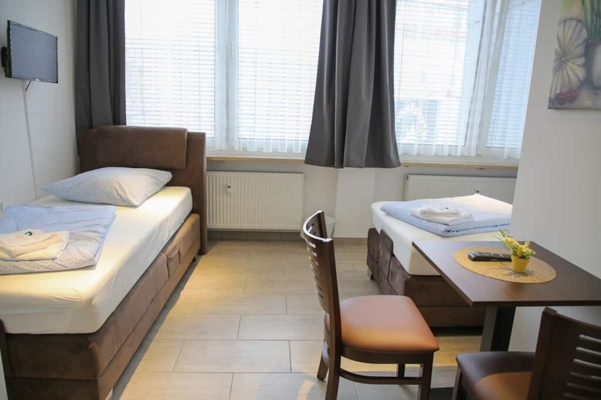 A compact bedroom with a single bed, a small table, and a chair.